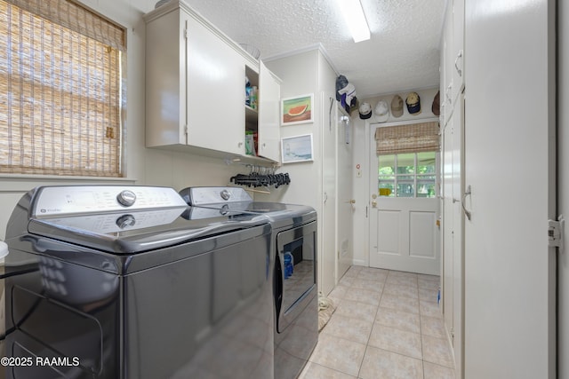 laundry area featuring a textured ceiling, cabinet space, light tile patterned floors, and washing machine and dryer