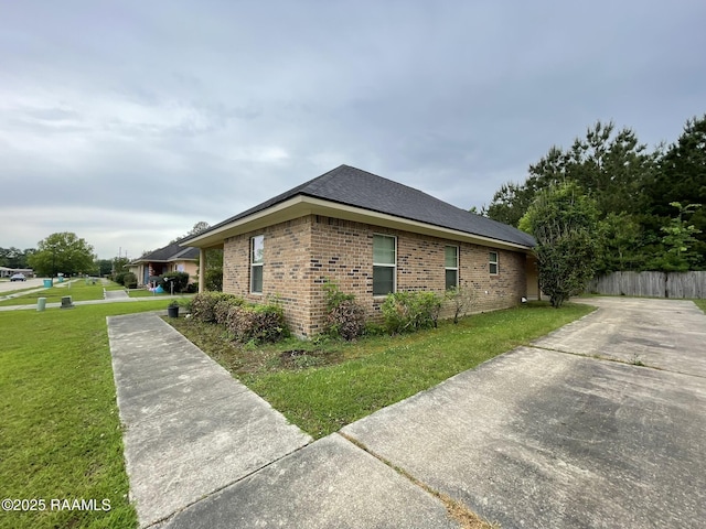 view of side of home with a lawn, brick siding, fence, and roof with shingles