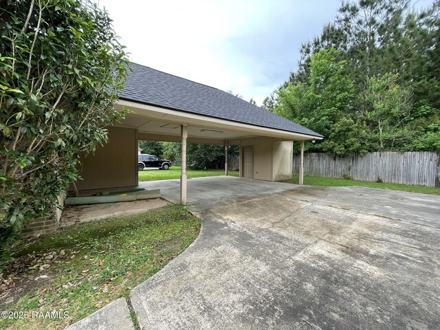 view of parking / parking lot featuring concrete driveway and fence