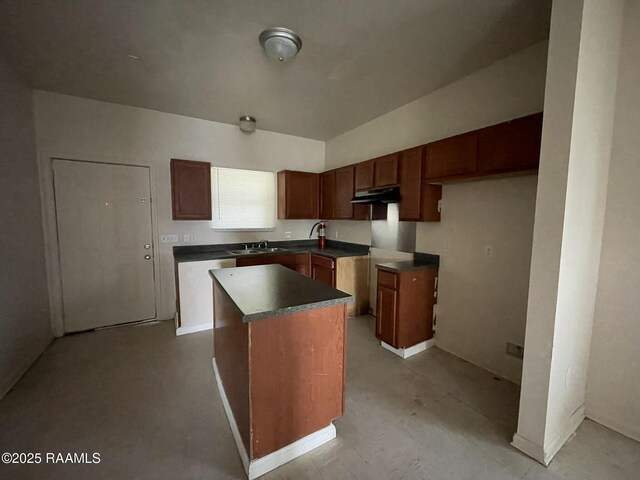 kitchen featuring dark countertops, a kitchen island, under cabinet range hood, and a sink