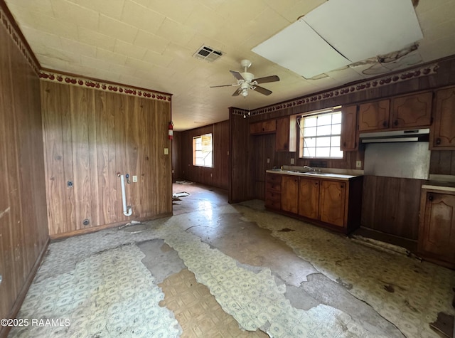 kitchen with light floors, ceiling fan, under cabinet range hood, and wooden walls