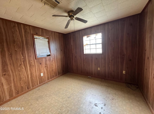 spare room featuring light floors, wood walls, a ceiling fan, and visible vents