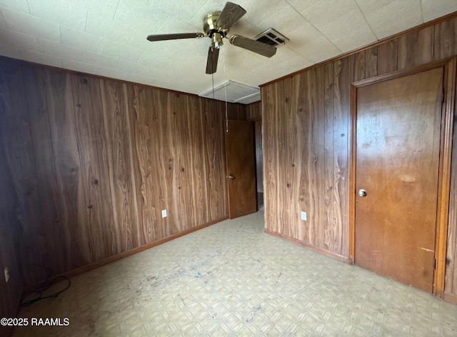 empty room with tile patterned floors, wood walls, visible vents, baseboards, and ceiling fan