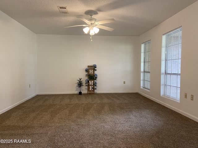 empty room featuring visible vents, baseboards, dark colored carpet, a textured ceiling, and a ceiling fan
