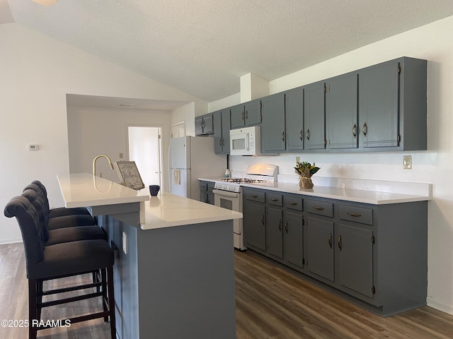 kitchen featuring white appliances, dark wood-style floors, light countertops, a textured ceiling, and vaulted ceiling
