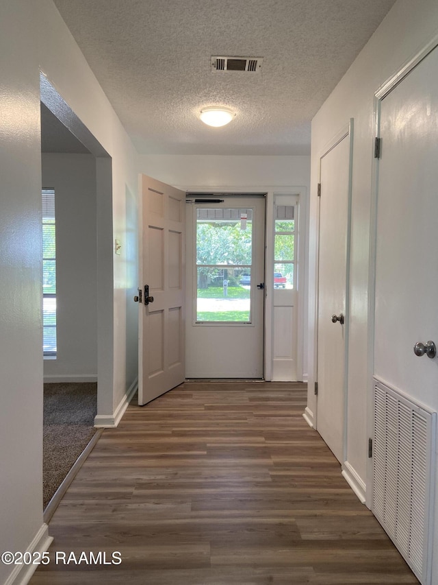 hall with a textured ceiling, baseboards, wood finished floors, and visible vents