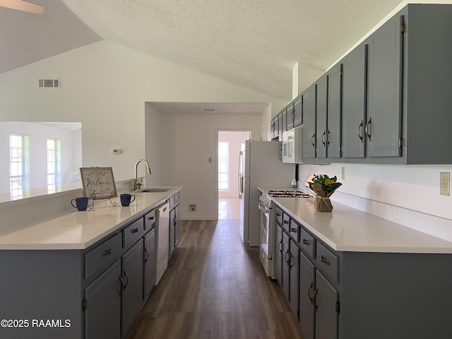 kitchen featuring a sink, vaulted ceiling, white appliances, and visible vents