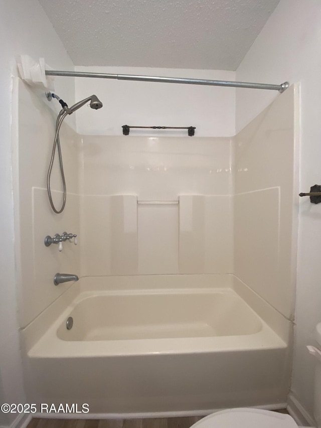 full bathroom featuring bathtub / shower combination, toilet, and a textured ceiling