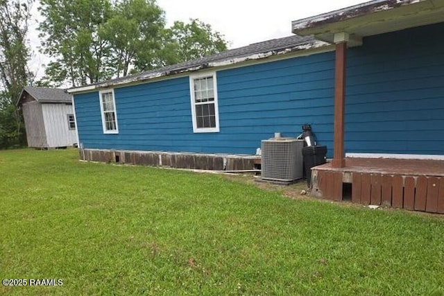 view of side of home with an outdoor structure, a yard, central AC, and a shed