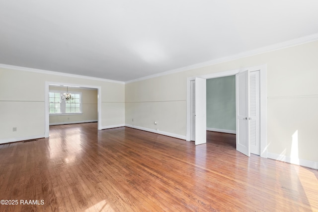 empty room featuring a chandelier, ornamental molding, and wood finished floors