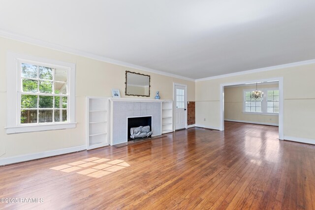 unfurnished living room featuring a fireplace, a notable chandelier, crown molding, baseboards, and wood finished floors