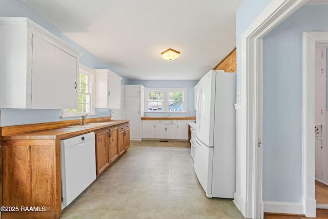 kitchen featuring light floors, a sink, white cabinets, and white appliances