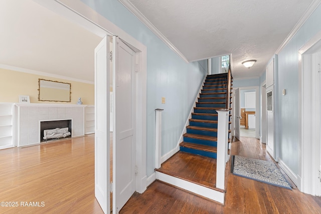 stairway with crown molding, baseboards, wood finished floors, and a fireplace