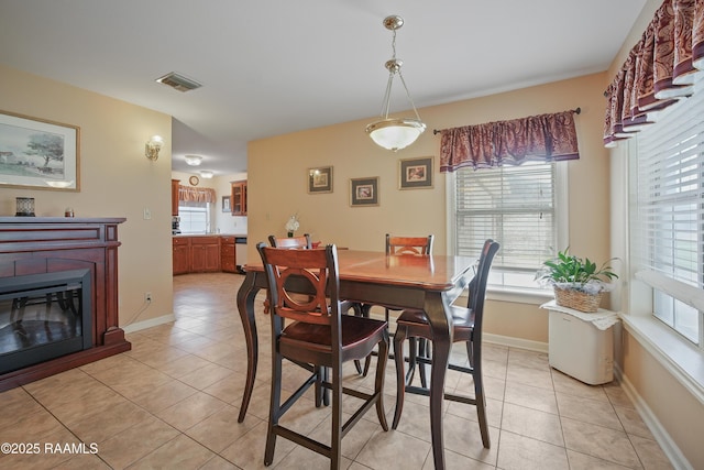 dining room with light tile patterned flooring, visible vents, a glass covered fireplace, and baseboards