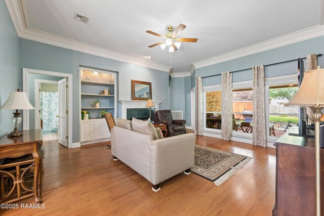 living area featuring crown molding, visible vents, a premium fireplace, wood finished floors, and a ceiling fan