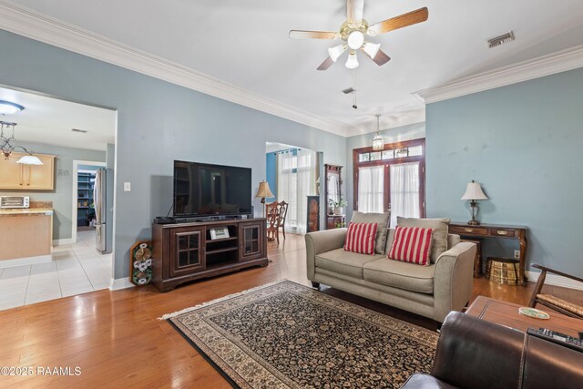 living area featuring ornamental molding, light wood finished floors, a ceiling fan, and visible vents