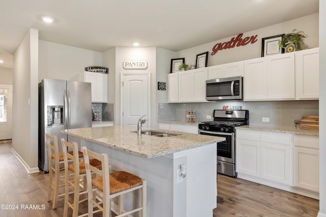 kitchen featuring a sink, light wood-style flooring, backsplash, appliances with stainless steel finishes, and an island with sink