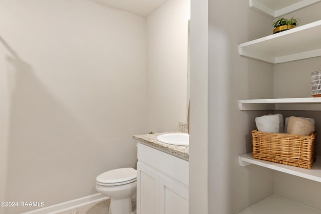 half bathroom featuring toilet, tile patterned flooring, vanity, and baseboards