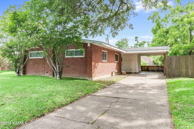 view of side of home with fence, brick siding, concrete driveway, a yard, and a carport