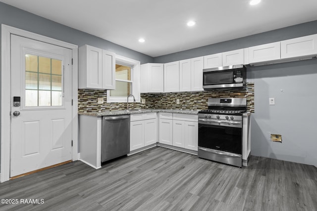kitchen with light wood-style floors, appliances with stainless steel finishes, white cabinets, and decorative backsplash