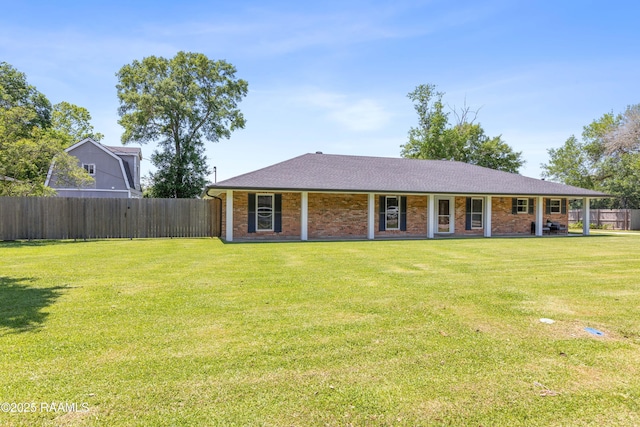 rear view of house featuring brick siding, roof with shingles, a yard, and fence