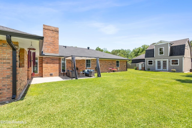 back of house with a lawn, a shingled roof, a patio area, and a chimney