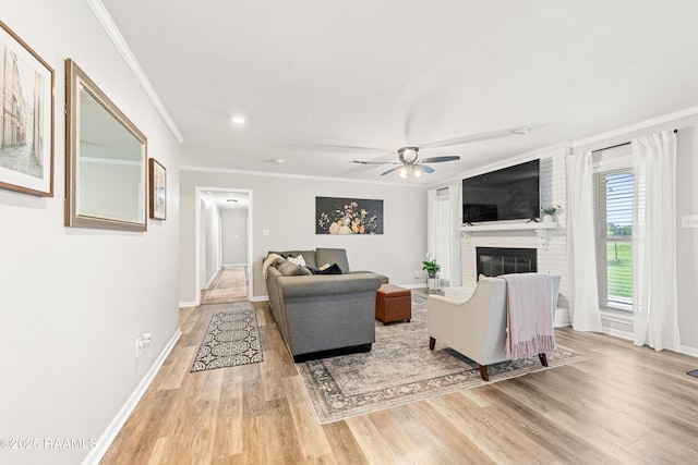 living room with ornamental molding, ceiling fan, a brick fireplace, baseboards, and light wood-type flooring