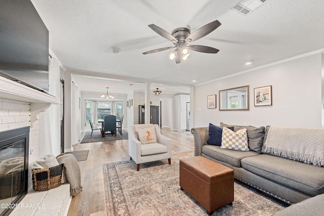 living area featuring light wood-style floors, a brick fireplace, a ceiling fan, visible vents, and a textured ceiling