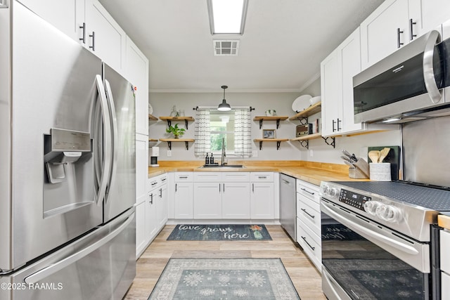 kitchen featuring appliances with stainless steel finishes, open shelves, light wood finished floors, and a sink