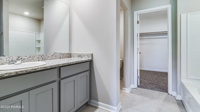 full bath featuring vanity, a bathtub, toilet, baseboards, and a spacious closet