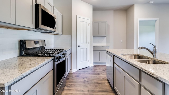 kitchen with gray cabinets, wood finished floors, light stone counters, stainless steel appliances, and a sink