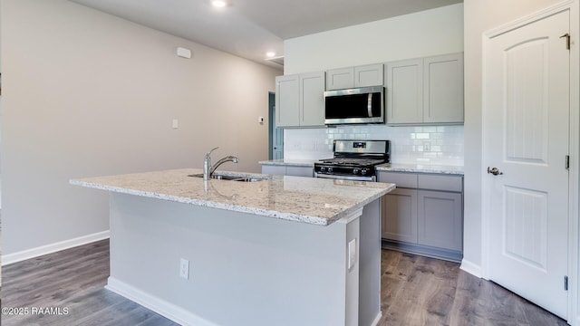 kitchen with a sink, backsplash, gray cabinetry, appliances with stainless steel finishes, and an island with sink