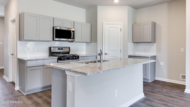kitchen featuring a sink, light stone counters, baseboards, gray cabinetry, and appliances with stainless steel finishes
