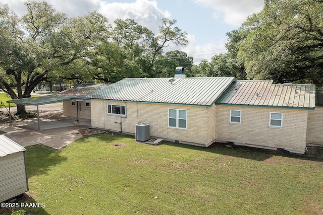 back of house with metal roof, a chimney, brick siding, central AC, and a yard