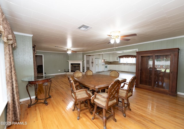 dining area with a glass covered fireplace, ceiling fan, ornamental molding, and visible vents