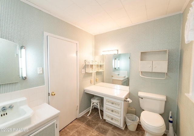 bathroom featuring ornamental molding, toilet, tile walls, baseboards, and a sink