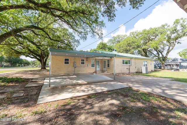 back of house with brick siding, cooling unit, a yard, entry steps, and an attached carport