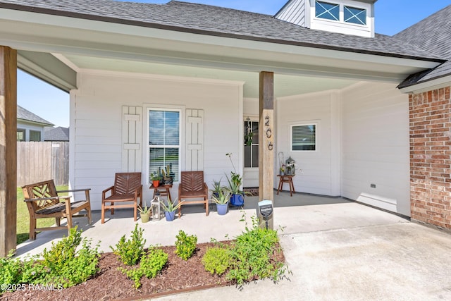 entrance to property featuring covered porch, brick siding, fence, and a shingled roof
