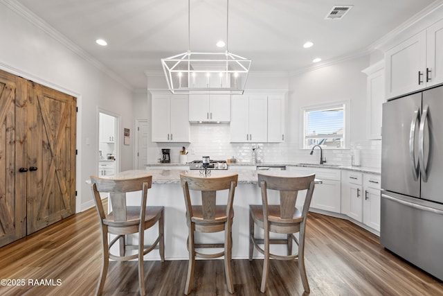 kitchen with a kitchen island, white cabinetry, stainless steel refrigerator, and a sink