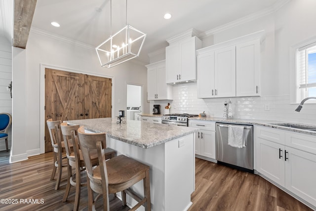 kitchen with a kitchen island, a sink, ornamental molding, stainless steel appliances, and white cabinetry