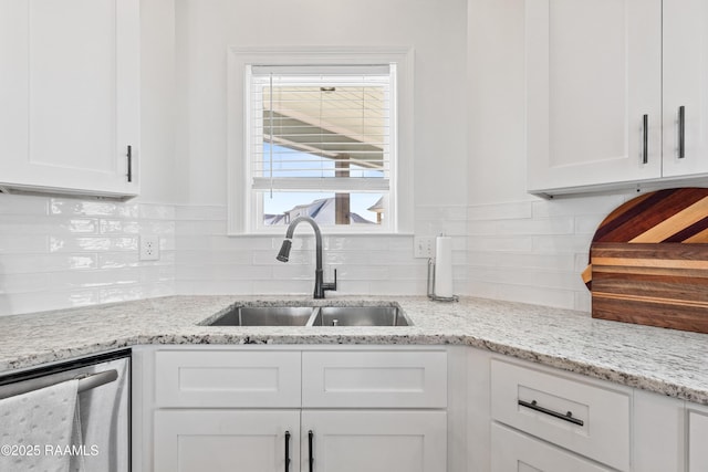 kitchen featuring stainless steel dishwasher, a sink, decorative backsplash, and white cabinets