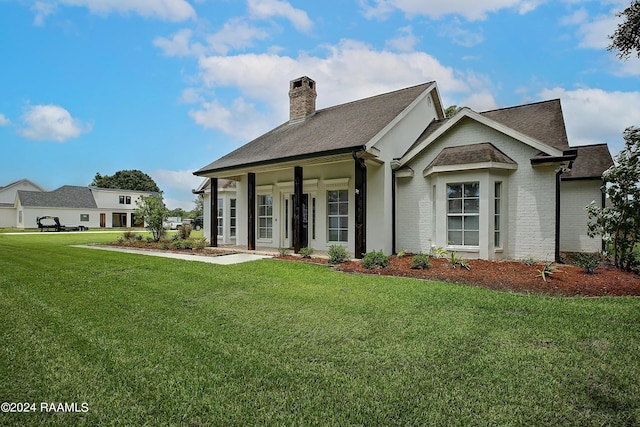 view of front of house with roof with shingles, a chimney, a front yard, and brick siding
