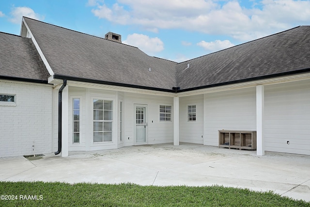 rear view of property with a chimney, a patio area, and a shingled roof