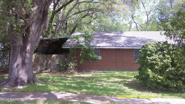 view of property exterior featuring fence, a shingled roof, a yard, and brick siding