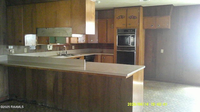 kitchen with brown cabinets, a sink, light countertops, a peninsula, and black appliances