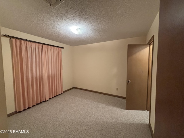 empty room featuring a textured ceiling, light colored carpet, and baseboards