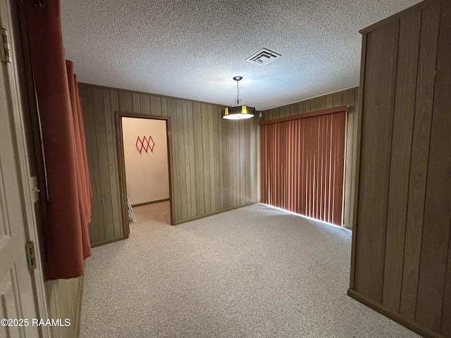 carpeted empty room featuring wooden walls, a textured ceiling, and visible vents