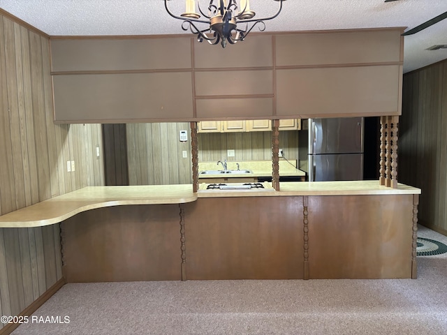 kitchen featuring wood walls, light countertops, freestanding refrigerator, an inviting chandelier, and carpet flooring