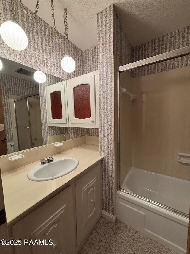 bathroom featuring a textured ceiling, wallpapered walls, bath / shower combo with glass door, and vanity