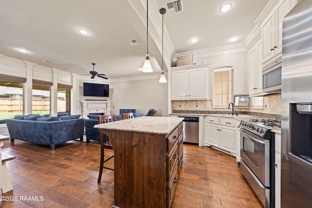 kitchen with visible vents, crown molding, a kitchen bar, a ceiling fan, and appliances with stainless steel finishes